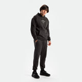 a fit man stand at right and wearing matching set pirate black ,hoodie and pants ,plus shoes black 