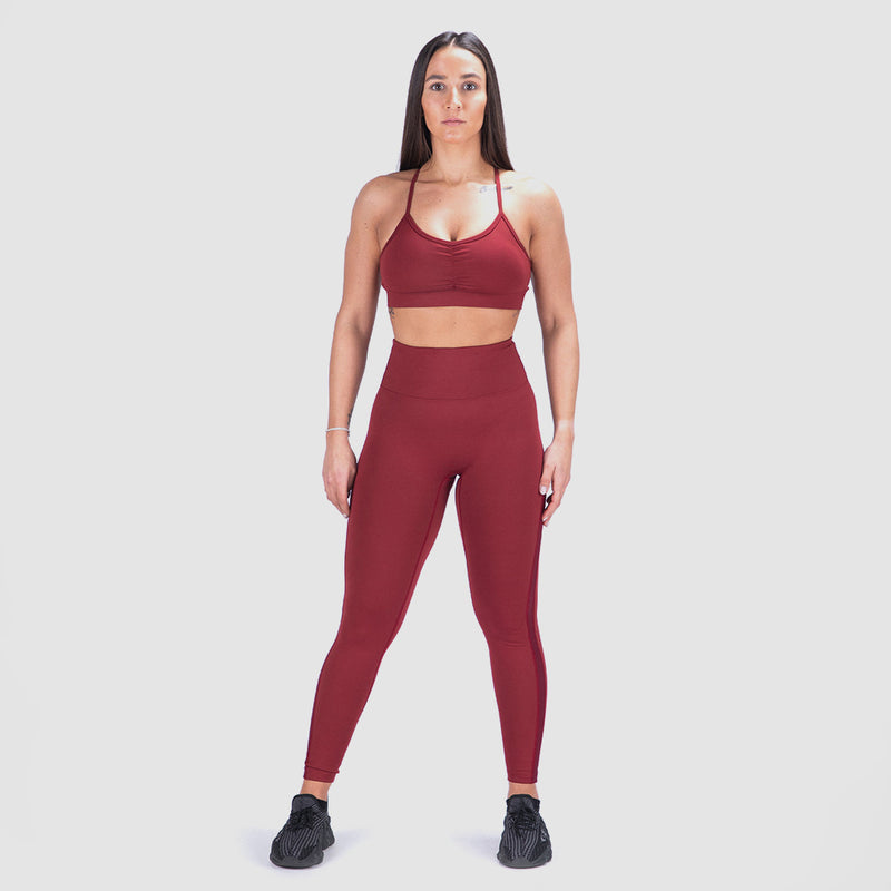 a fit woman wearing matching bra and legging red ,with shoes black ,she look at the camera ,the background is light grey 