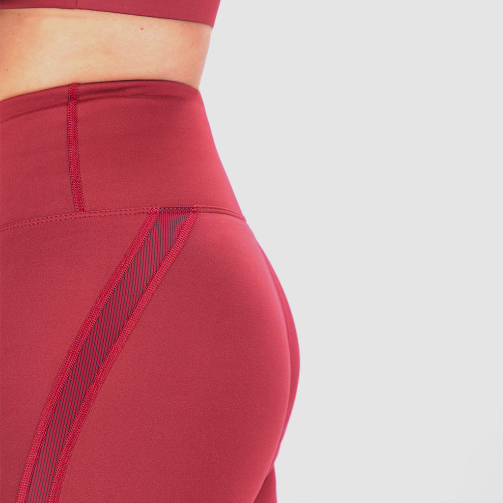 A close-up of a person wearing high-waisted red leggings with mesh panel details, paired with a matching sports bra, against a light  gray background