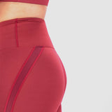 A close-up of a person wearing high-waisted red leggings with mesh panel details, paired with a matching sports bra, against a light  gray background