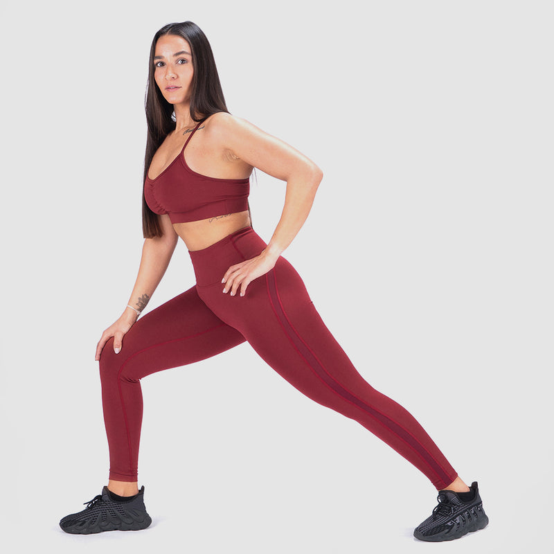 a woman stand with pose sport and wearing matching bra and legging red ,with shoes black, she look at the camera ,the background is light grey 