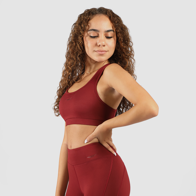 Woman wearing matching red bra and leggings, standing and looking to the right, against a light gray background