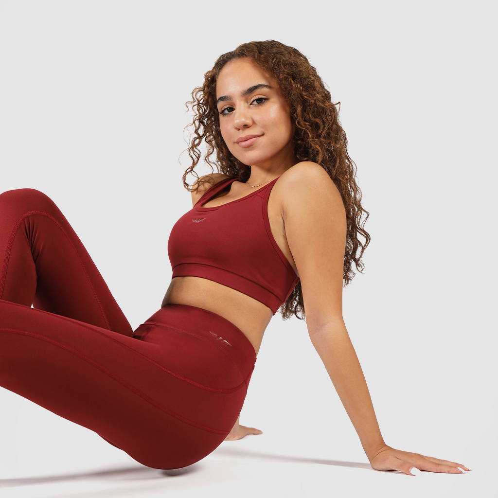 Woman wearing a red bra and matching leggings, sitting on the floor looking at the camera and smiling