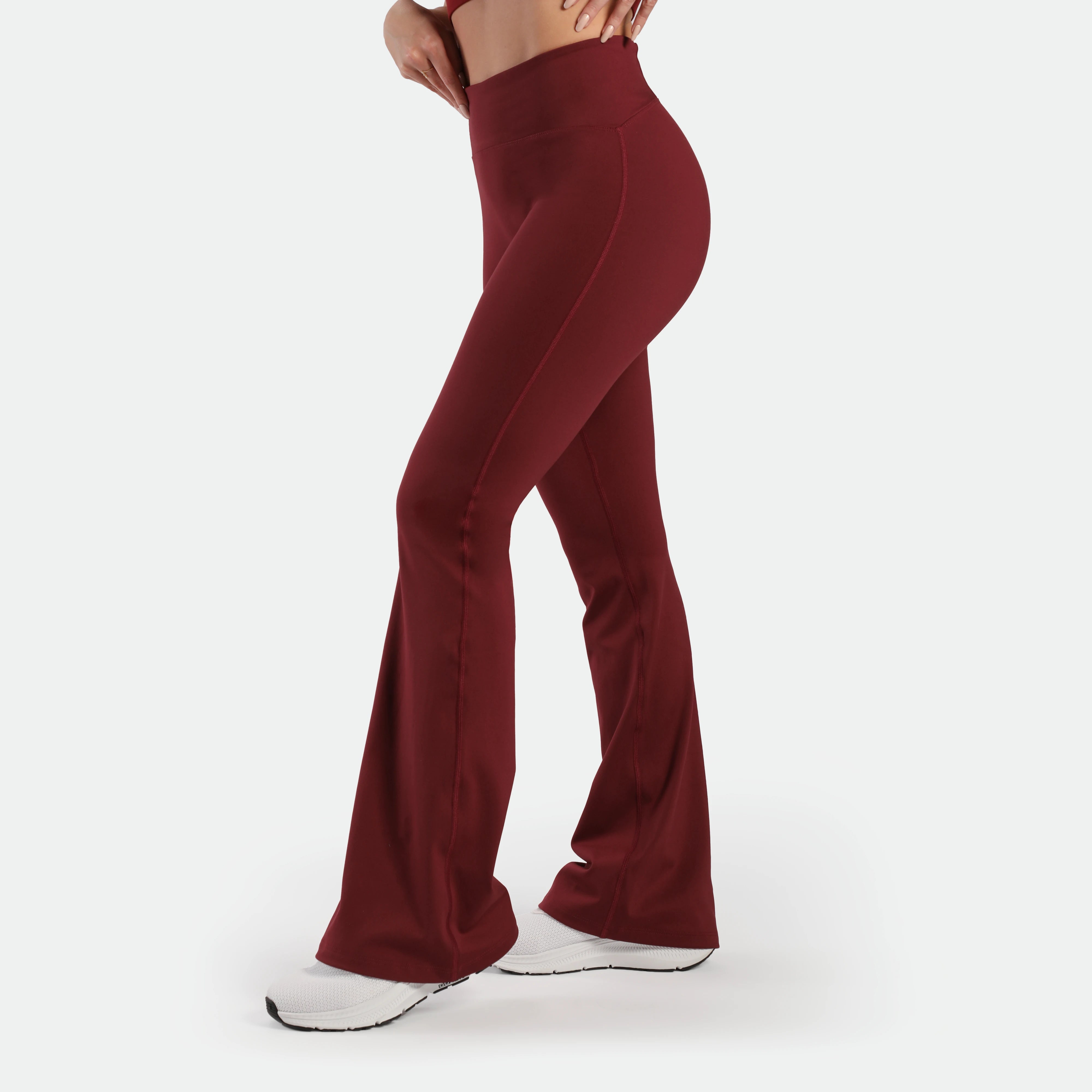 a fit woman stand at right and wearing flared legging pomegranate with shoes white  