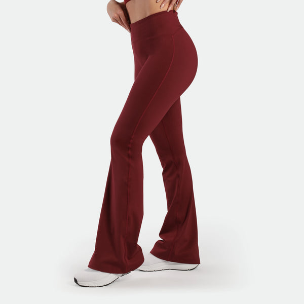 a fit woman stand at right and wearing flared legging pomegranate with shoes white  