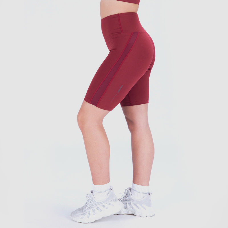 a fit woman stand at right and wearing seamless shot red with little mesh fabric and logo ,she wearing shoes with socks white ,plus the background is light grey  