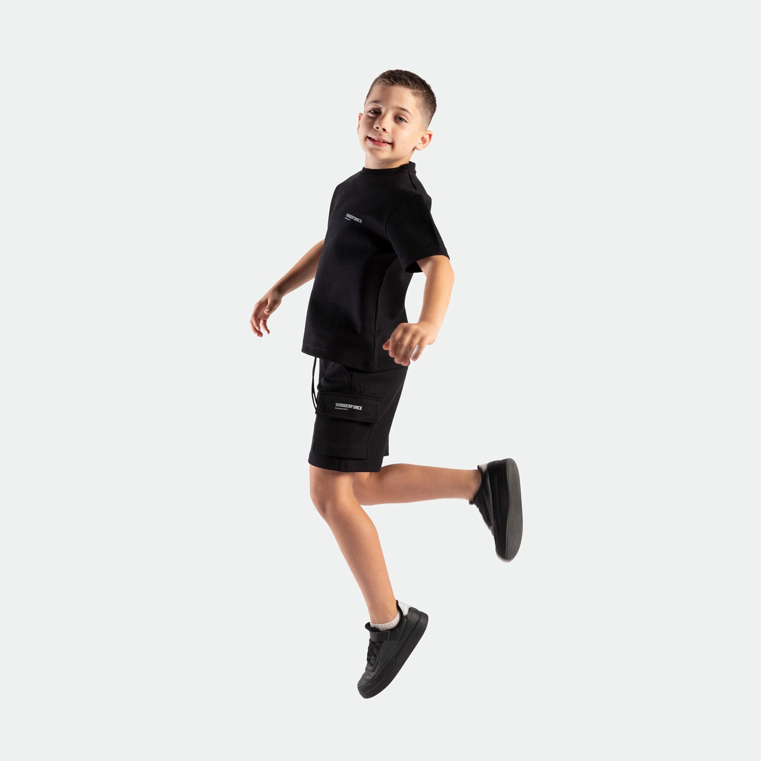 a fit boy stand at right and wearing matching set black ,t-shirt and short , plus shoes 