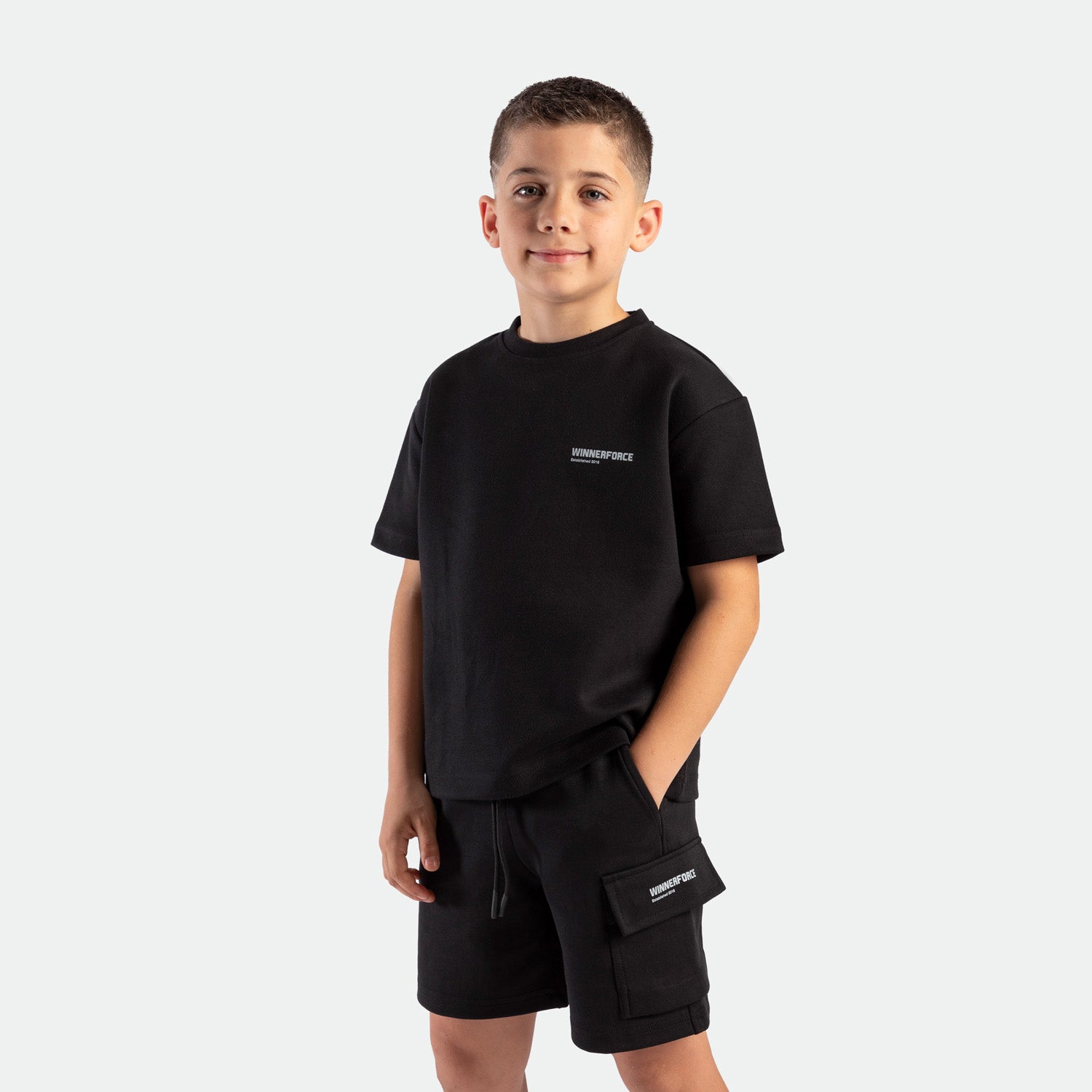 a young boy look at the camera and smile ,he wearing matching set black ,t-shirt and short  