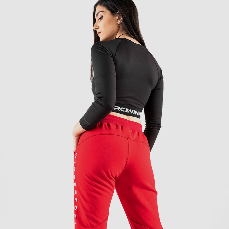a back view for fit woman wearing crop top black with logo and red jogger pants  ,plus the background is light grey 