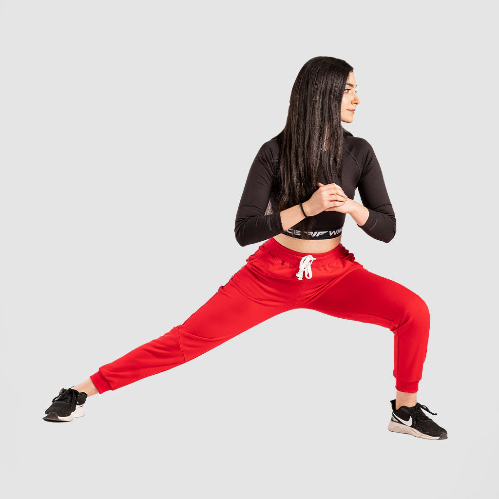a fit woman stand with pose sports and she wearing crop top  black with pants red and sneakers black 