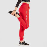 a fit  woman stand at right with pose sports and she wearing pants red with sneakers 