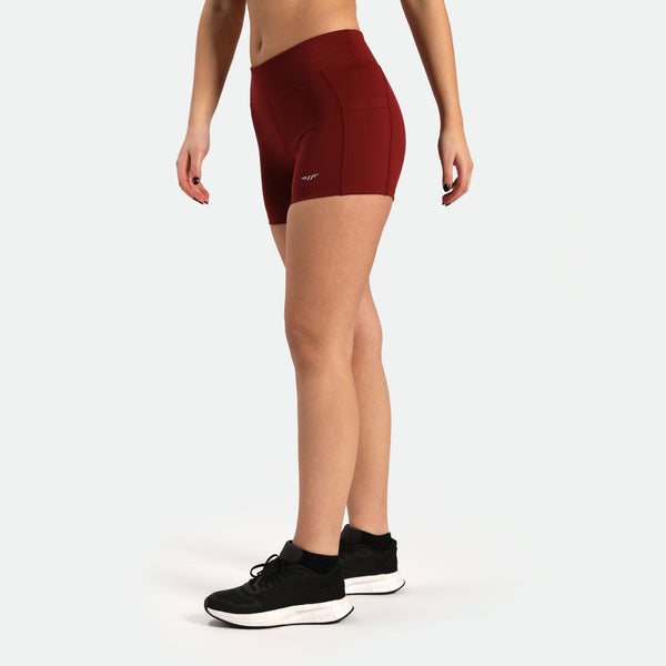 a fit woman stand at right and wearing short red with logo ,and she wearing shoes black ,plus the background is light grey 