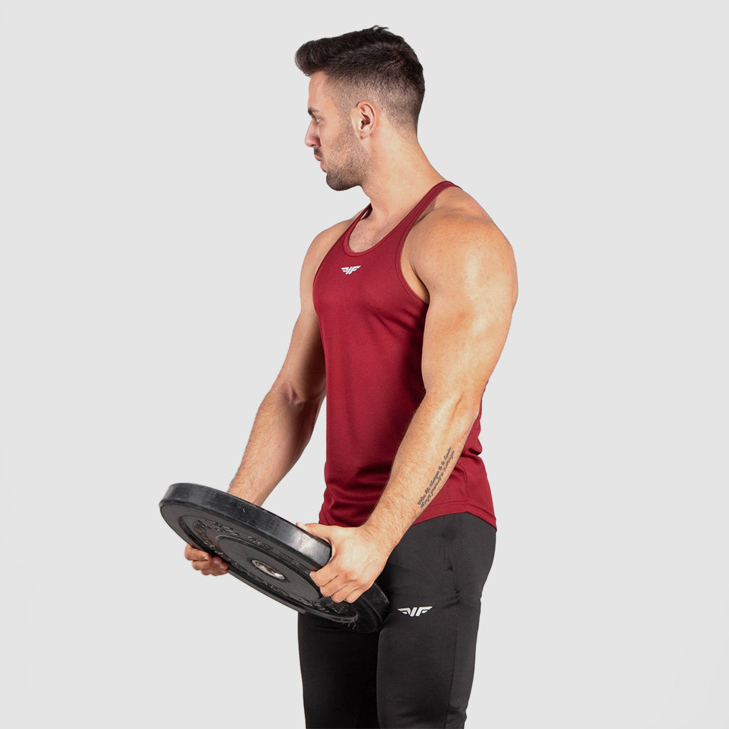 Man in red tank top and black pants holds a weight plate, facing left. Appears focused and fit, set against a neutral background. Fitness theme.