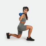 a fit woman stand with pose sports ,she wearing matching sage grey ,bra and short 