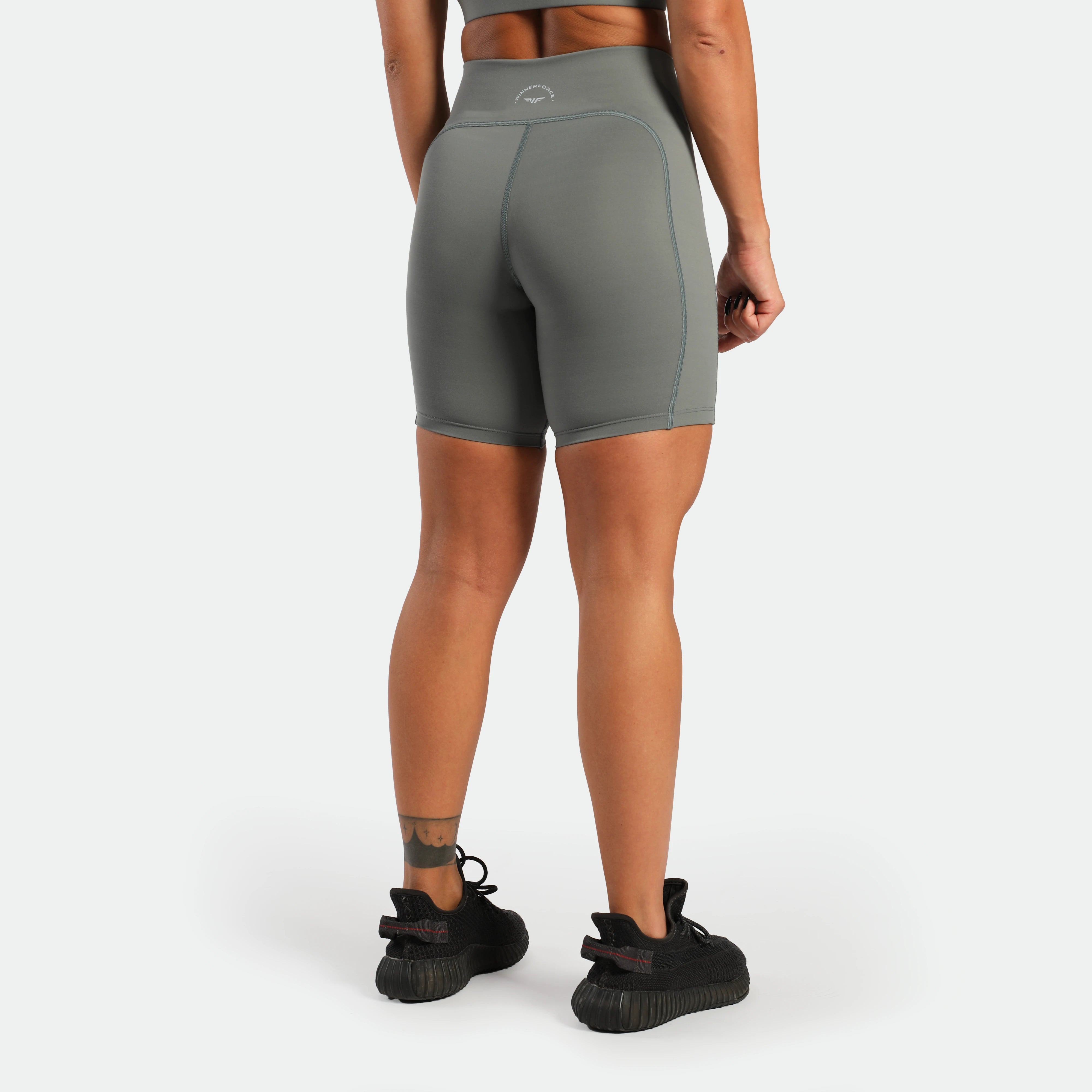 a back view for fit woman wearing short sage grey ,plus the shoes is black 