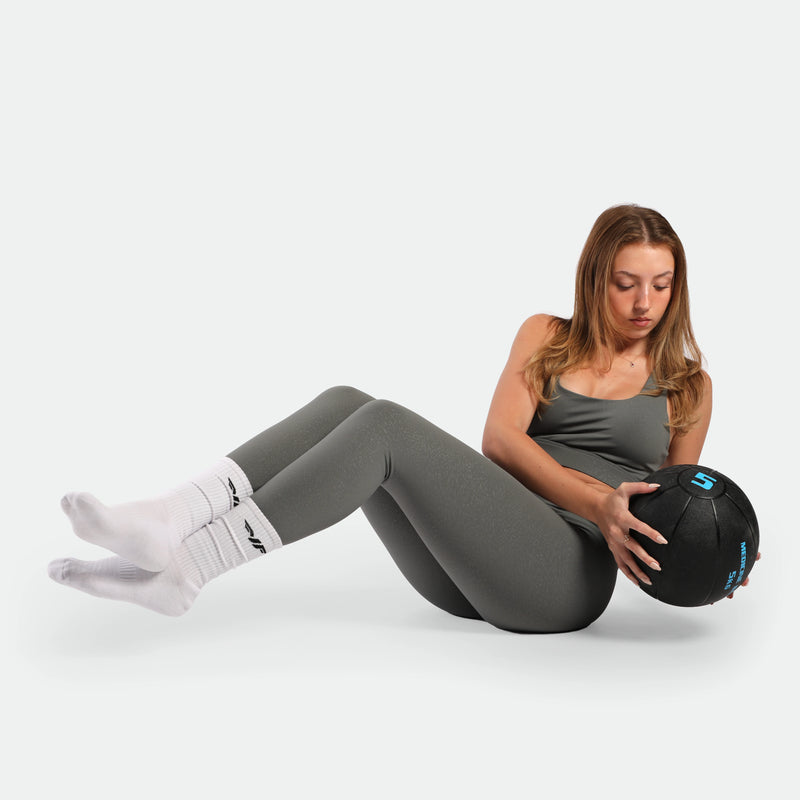 Woman exercising with a medicine ball on a white background ,she wearing matching set sage grey terrazzo blue  plus the sucks white 