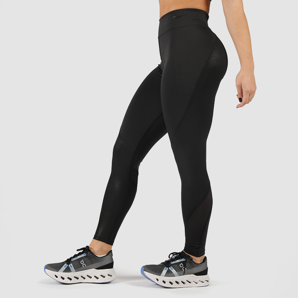 a fit woman stand at right and wearing legging black with shoes ,plus the background is light grey 