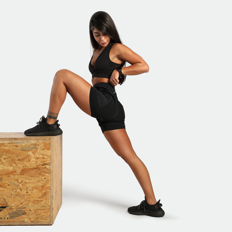 Woman in black athletic wear posing on a wooden box against a white background