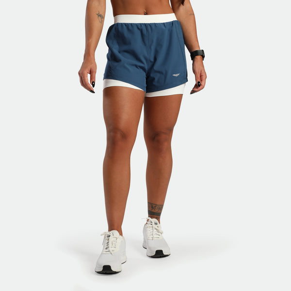 Person wearing blue athletic shorts with white accents on a white background