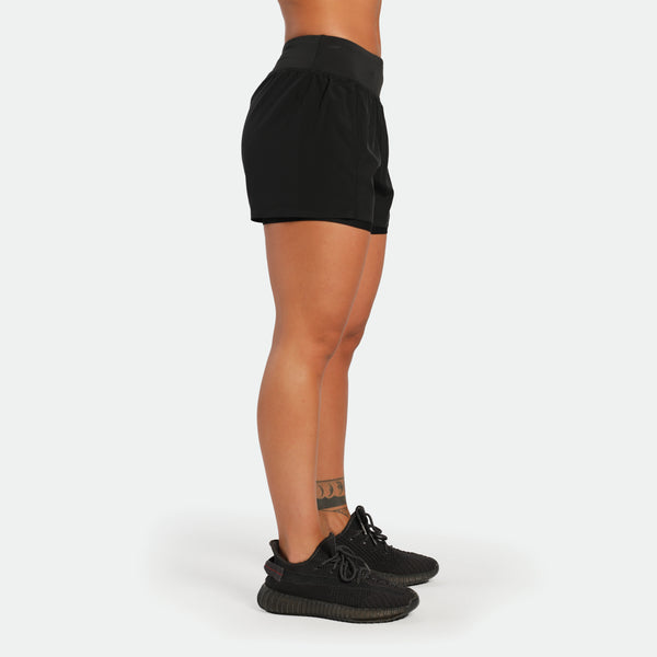Person wearing black shorts and black sneakers on a white background