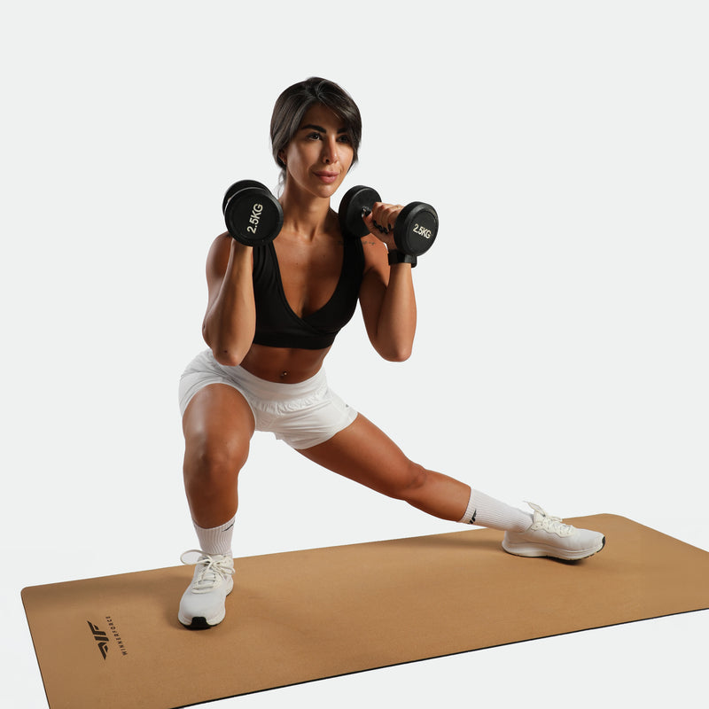 Woman exercising with dumbbells on a beige mat against a white background