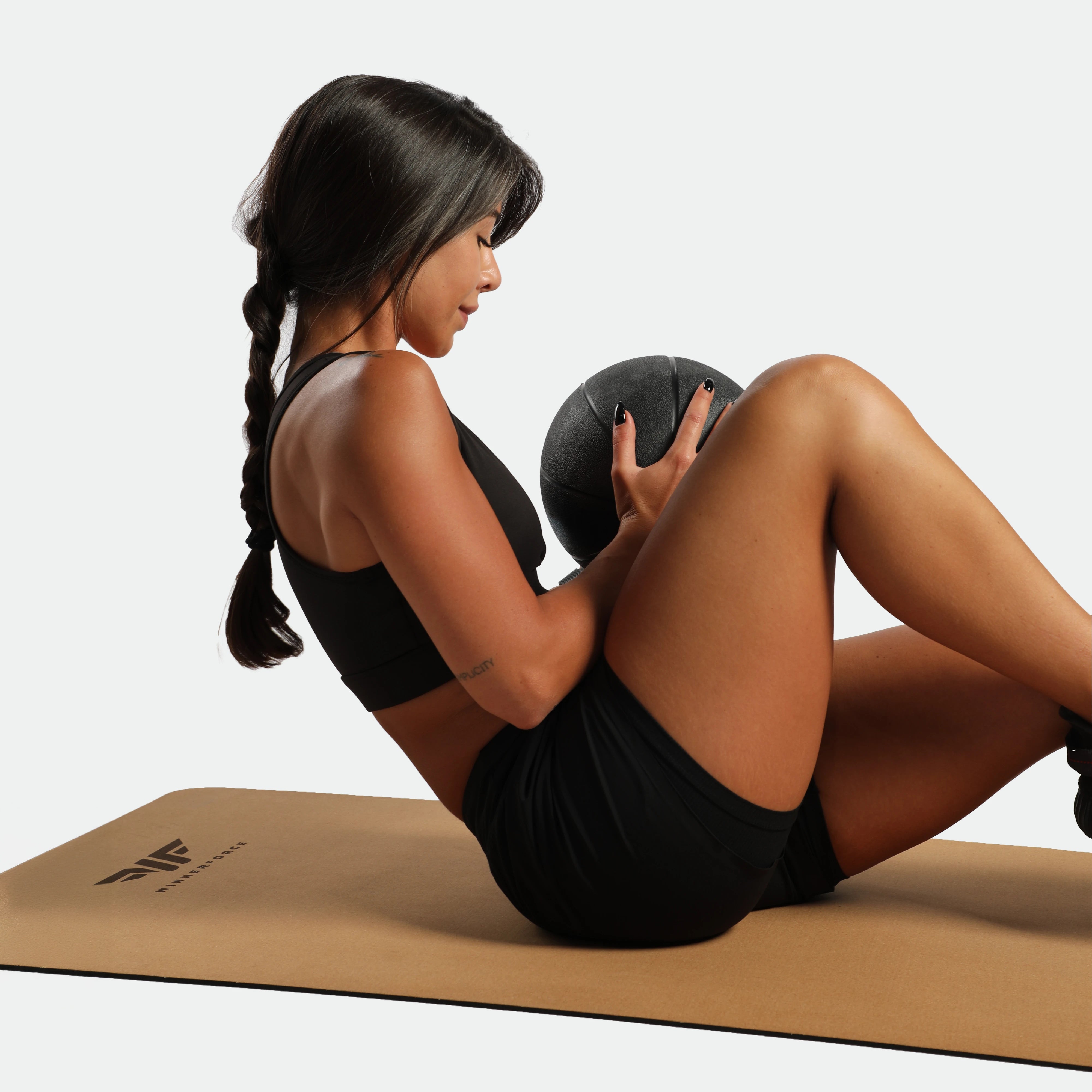 Woman exercising with a medicine ball on a mat against a plain background