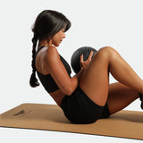 Woman exercising with a medicine ball on a mat against a plain background