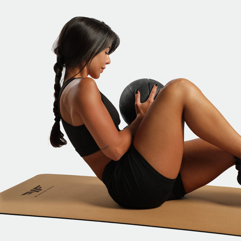 Woman exercising with a medicine ball on a mat against a plain background
