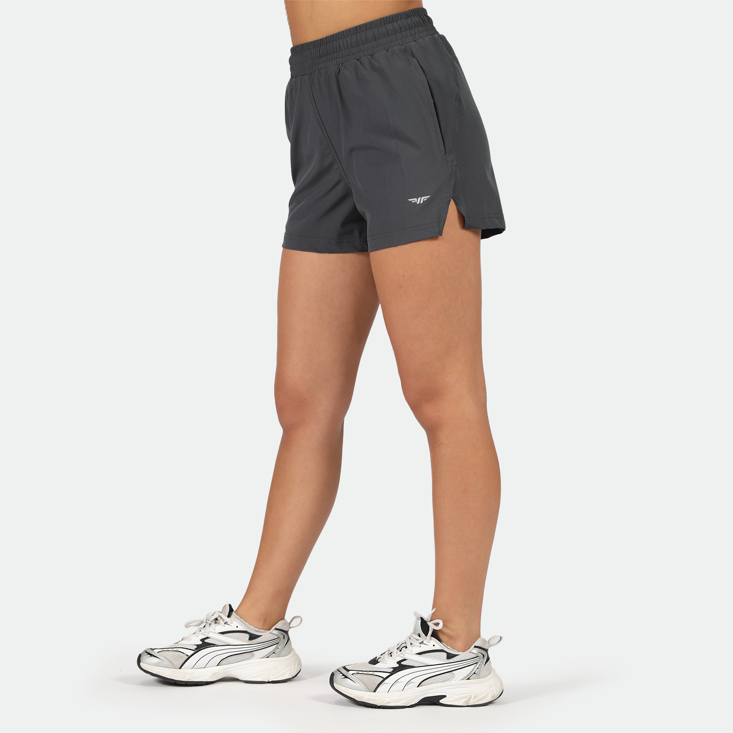 a fit woman stand at right  and wearing short grey with shoes ,plus the background is light grey 