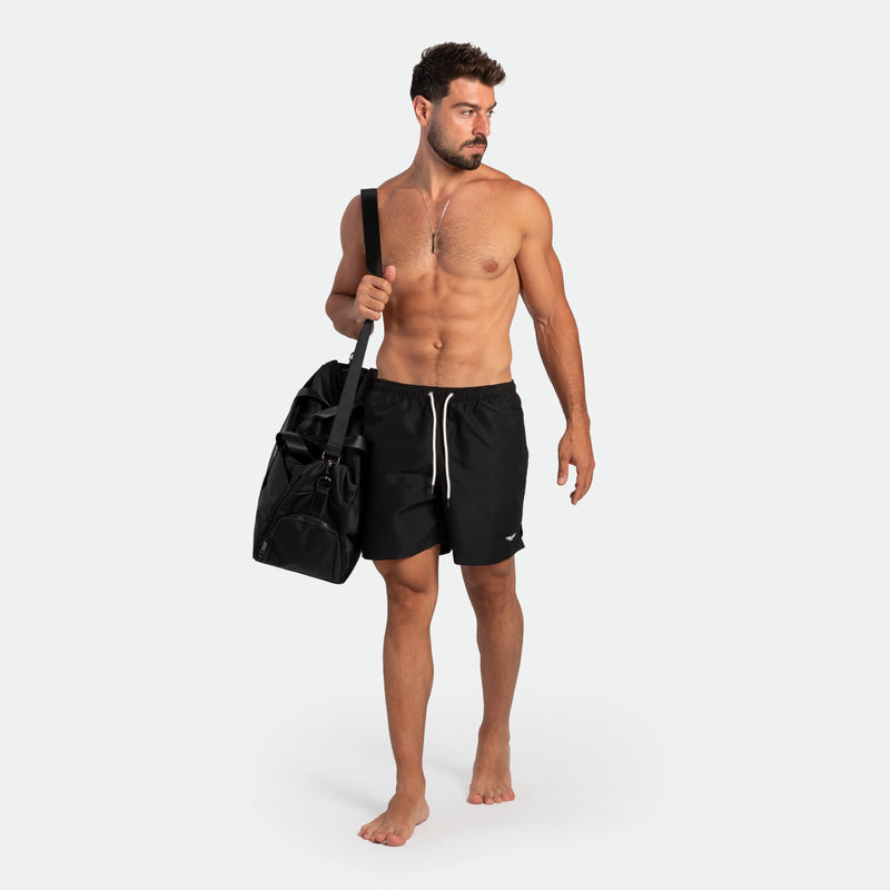 a fit man stand with pose and wearing short black plus the bag black 
