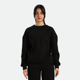 A young woman stands facing forward, wearing a black sweatshirt and black pants, against a plain white background.