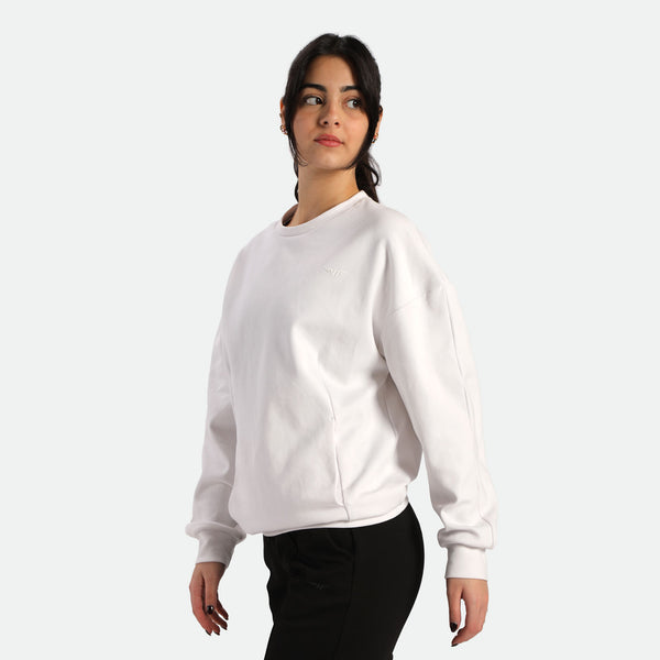 A person wearing a casual oversized white sweatshirt and black pants, standing against a plain background.