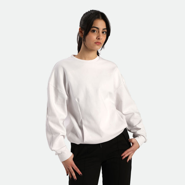 A person wearing a white oversized sweatshirt and black pants, posed against a neutral background.