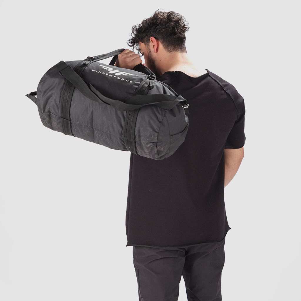 Man in a black t-shirt carrying a large black duffel bag over his shoulder, viewed from the back