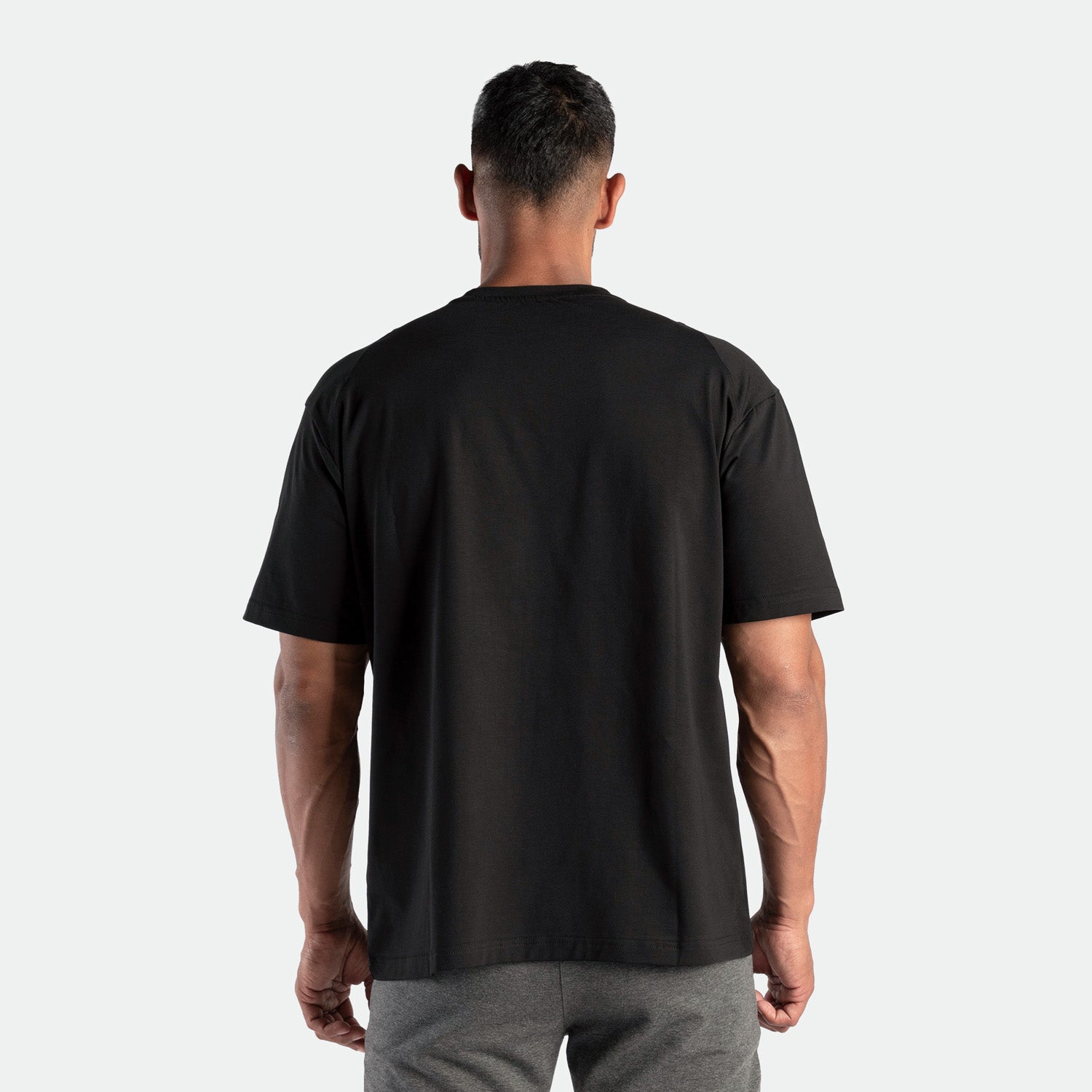 a back view for fit man wearing t-shirt black  and pants grey 