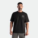 a fit man look at the camera and wearing t-shirt black with logo, plus the pants grey 