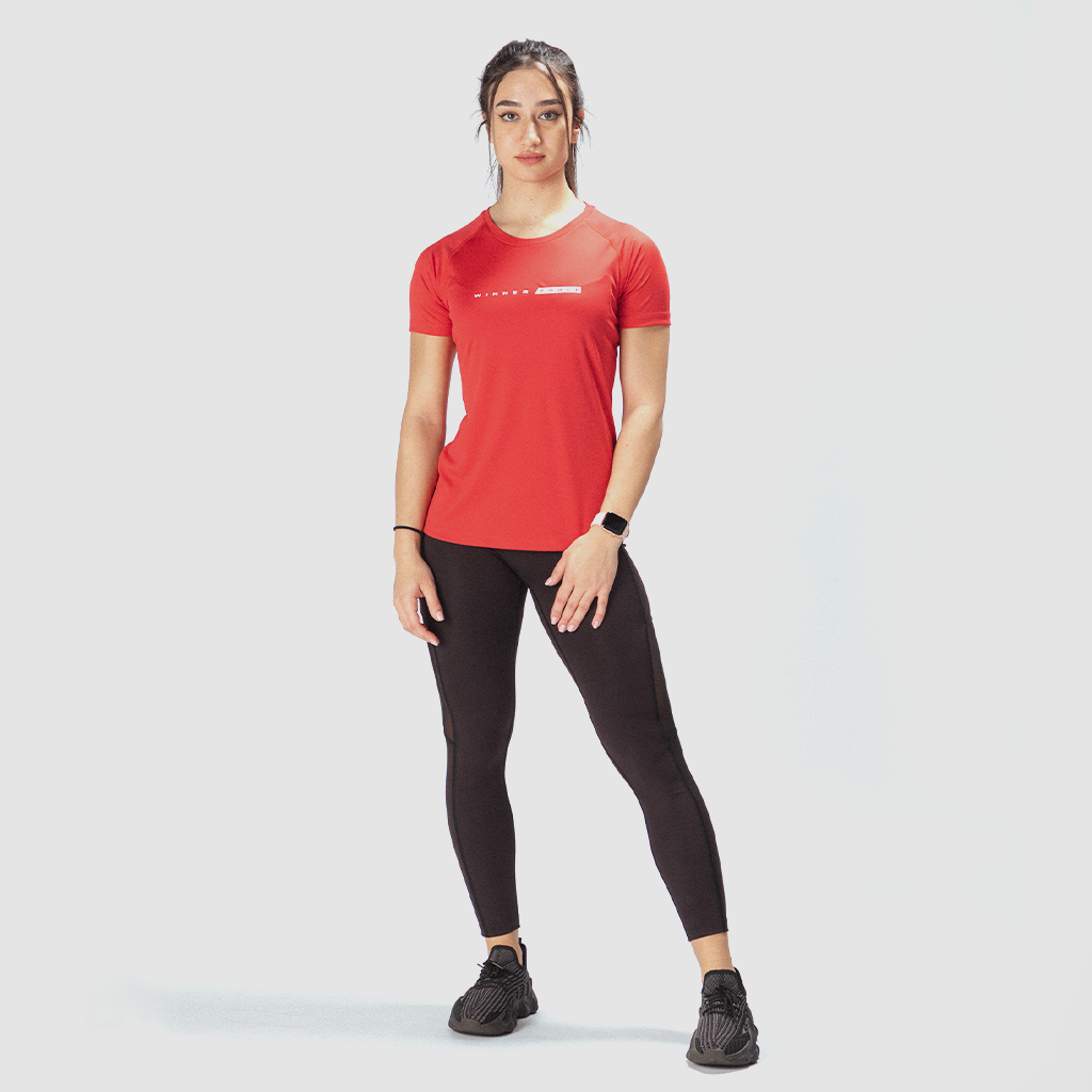 a fit woman look at the camera with confidence ,she wearing  t-shirt red  with logo and legging black ,plus she wearing  sneakers  black 