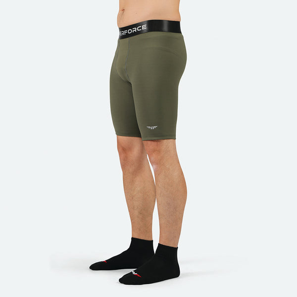 Man wearing olive green compression shorts with a black waistband, standing sideways. He is also wearing black socks. The background is plain white.