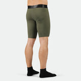 Man wearing olive green compression shorts with a black waistband, viewed from the back. He is barefoot against a plain white background.