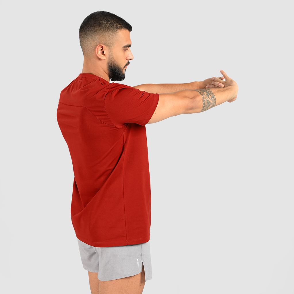 a fit man stand at right  with pose and he wearing t-shirt dark red with short grey 