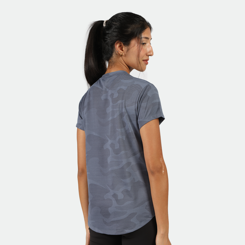 a back view for fit woman stand at right and look at down with smile ,she wearing camo t-shirt  blue with legging black 