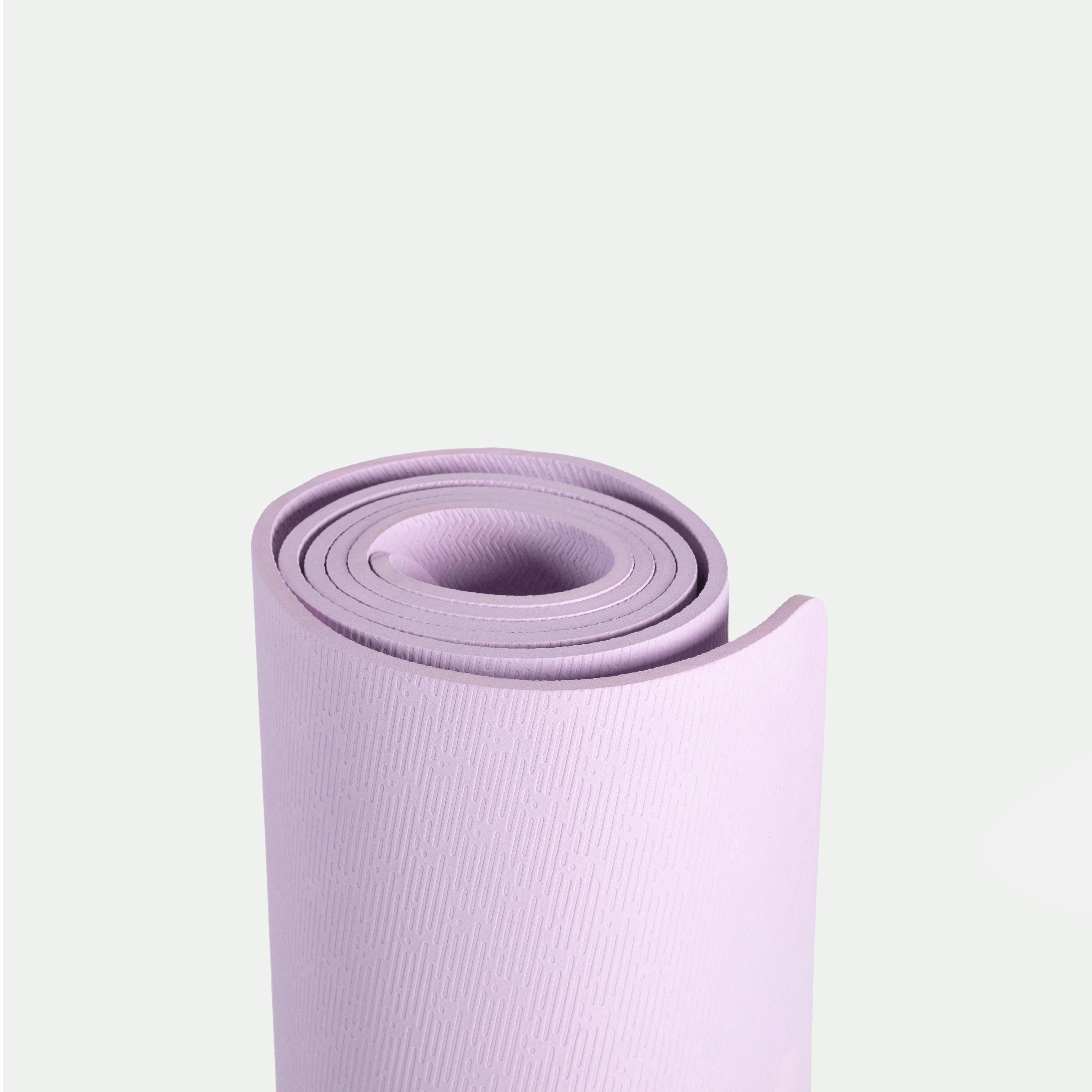 A rolled-up lavender yoga mat stands upright against a plain, light gray background. The mat is textured and features a subtle logo, giving a calm, minimalist feel.