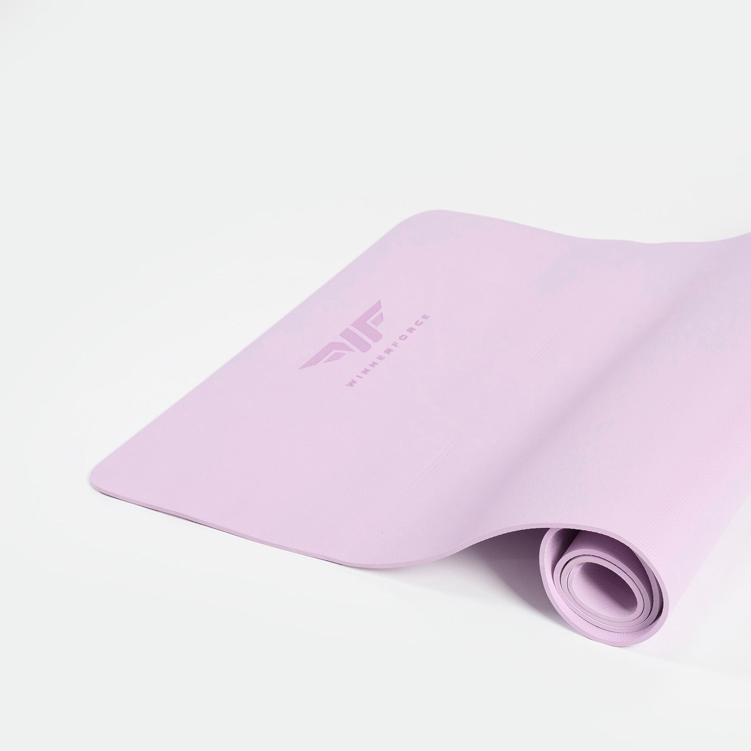 A pastel pink yoga mat partially rolled on a white surface, featuring a stylized logo and the word "WINNERFORCE." The scene is calm and minimalist