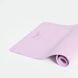 A pastel pink yoga mat partially rolled on a white surface, featuring a stylized logo and the word "WINNERFORCE." The scene is calm and minimalist