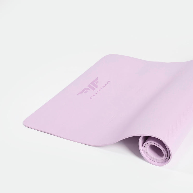 A pastel pink yoga mat partially rolled on a white surface, featuring a stylized logo and the word "WINNERFORCE." The scene is calm and minimalist