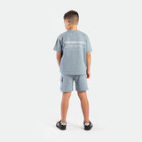 a back view for young boy wearing matching set dusty blue ,t-shirt  with logo and short with pocket ,plus the shoes