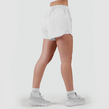 a fit woman stand at right and wearing short  white with shoes white ,plus the background is light grey 