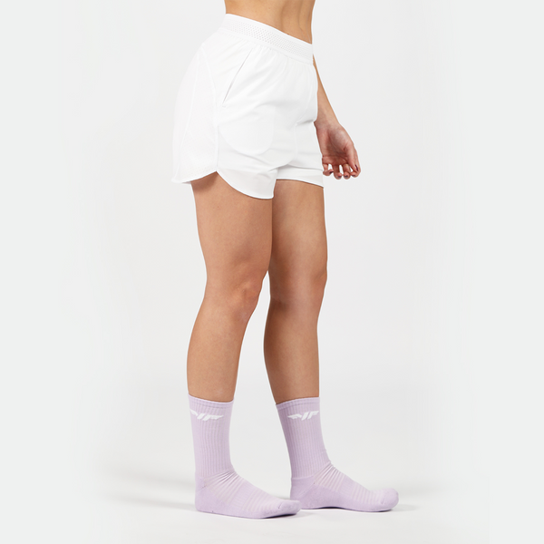 a fit woman stand at right and wearing short white with socks purpel ,plus the background is light grey 