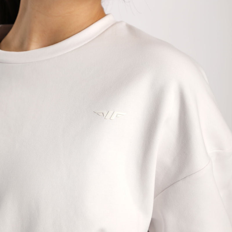 Close-up of a woman wearing a light-colored sweatshirt featuring a subtle embossed logo on the chest.