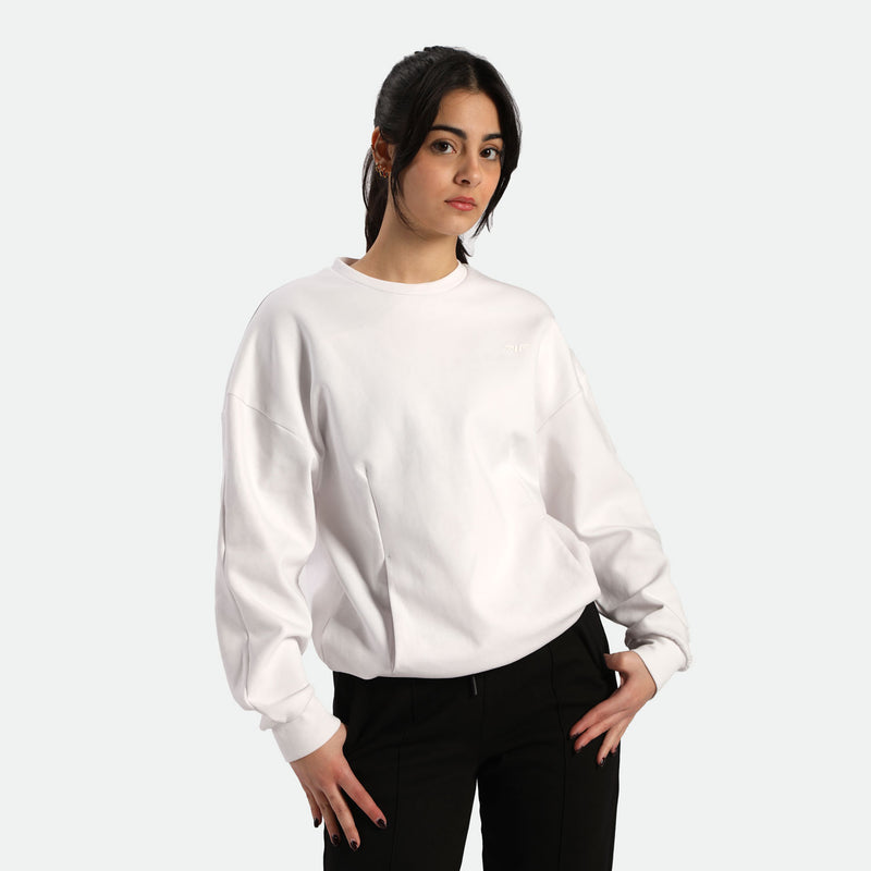 A person wearing a white oversized sweatshirt and black pants, posed against a neutral background.